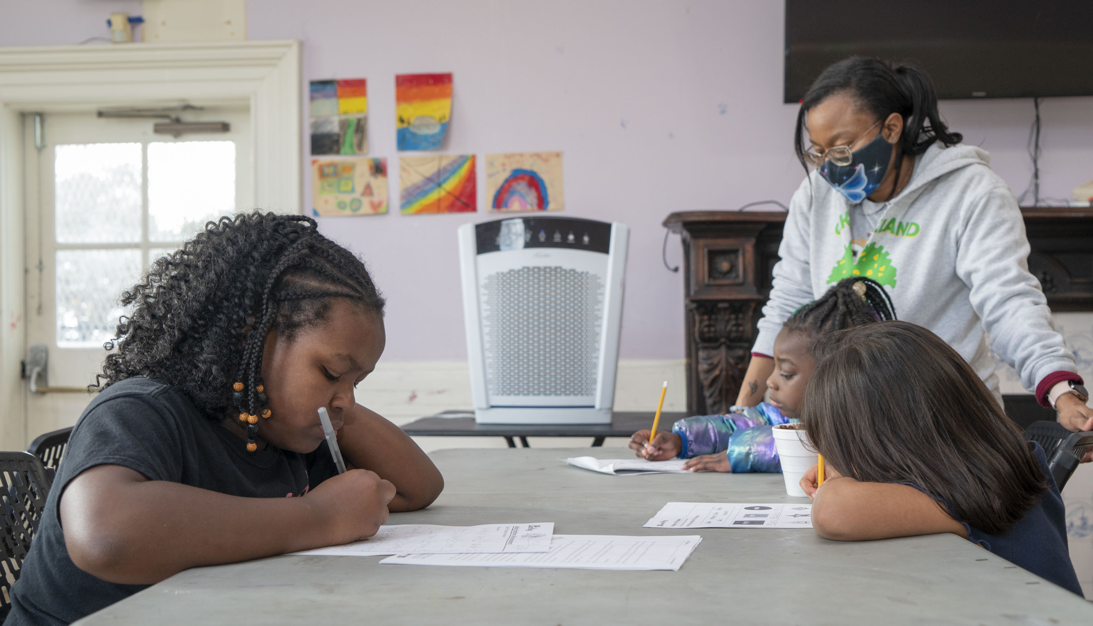 Three children working on an assignment with their teacher in a classroom with an air filter. 